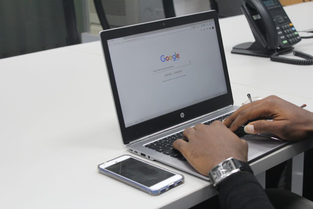 Open laptop on white tabletop, Google on the screen, phone and office chairs in background